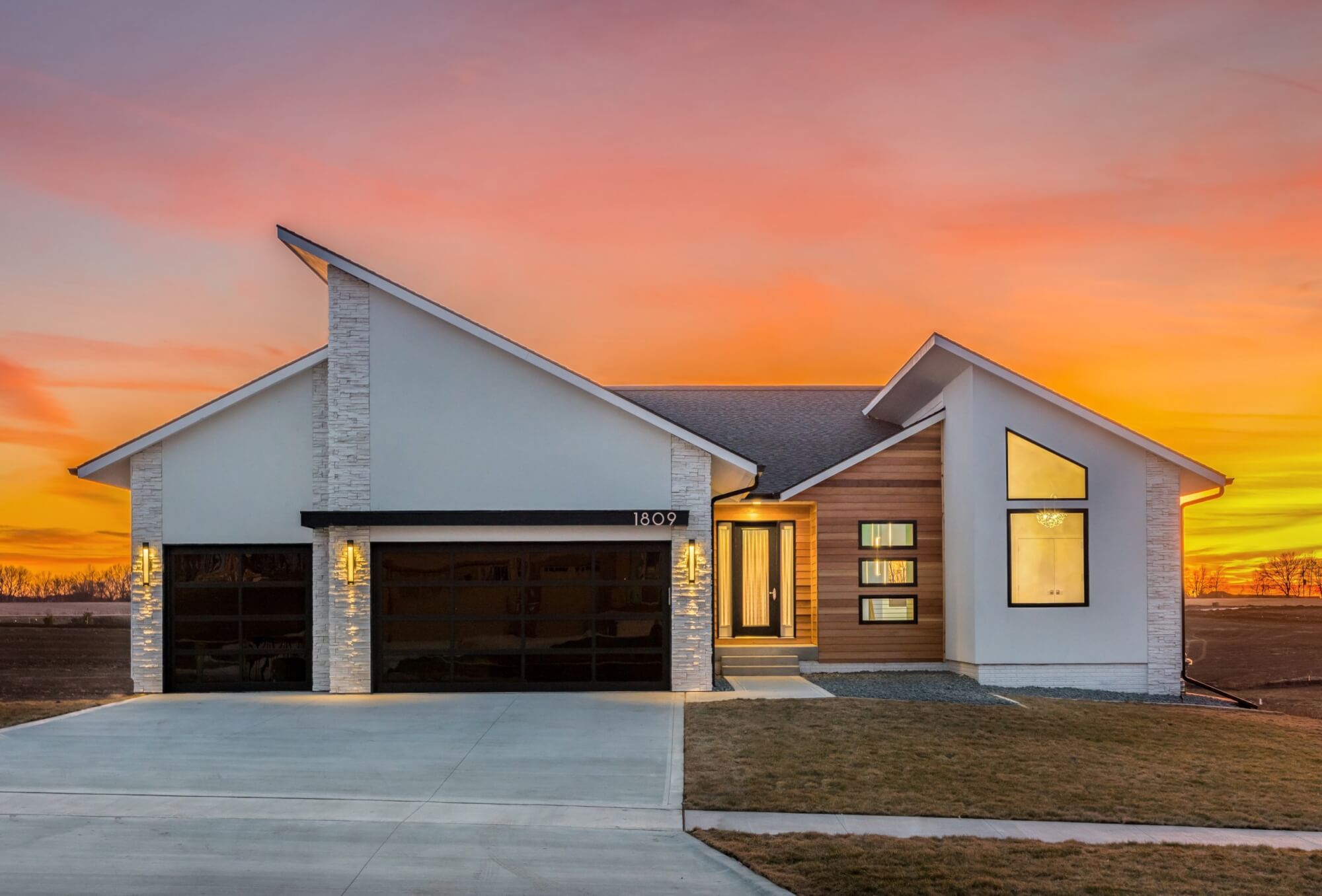 Modern-style custom-built home by Kruse Development with a white and wooden exterior, along with a sunset in the background.
